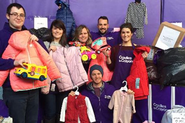 Volunteers in purple aprons collect children's items for a donation drive