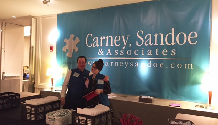 Two carney sandoe employees smile at conference check in
