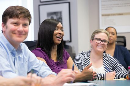 A man and three women smile in a staff meeting