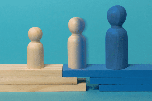 Three wooden game pieces, each gradually increasing in size, the left one is all wood color, the right one is all blue, and the middle one is half wood and half blue signaling transition