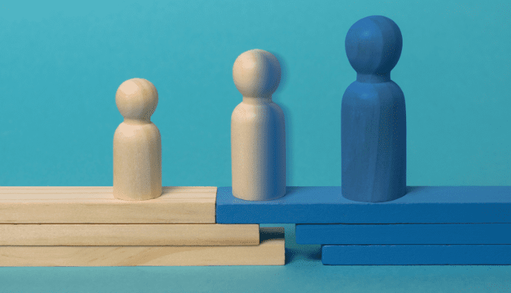 Three wooden game pieces, each gradually increasing in size, the left one is all wood color, the right one is all blue, and the middle one is half wood and half blue signaling transition