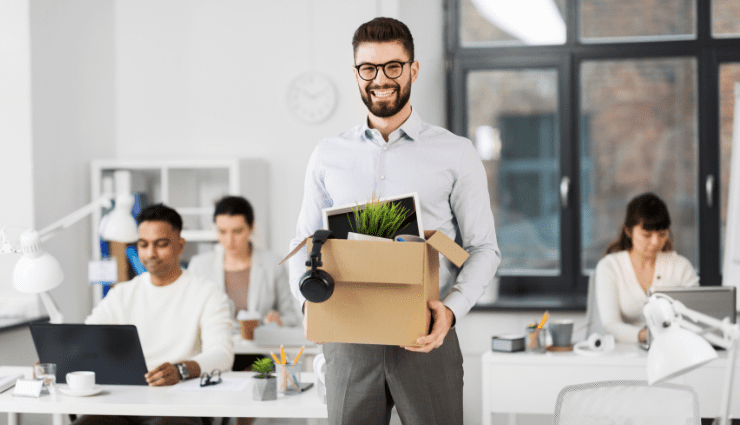 smiling young male businessman in an office holding a box of his desk items that he has packed up