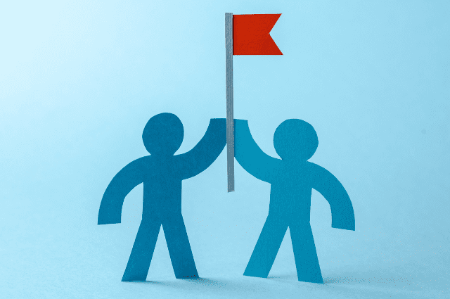 two paper cutouts of people holding up a red flag together in support