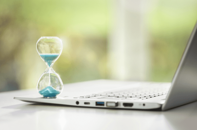 Hourglass with teal sand sitting next to an open laptop computer