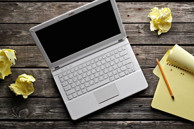 silver laptop with yellow paper crumpled and notepad with pencil