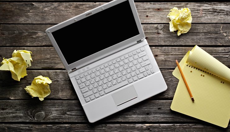 silver laptop with yellow paper crumpled and notepad with pencil