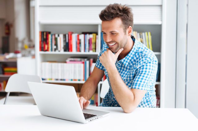 Man in gingham shirt smiling at laptop