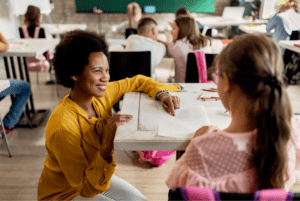 African American female teacher kneeling next to student sitting at desk