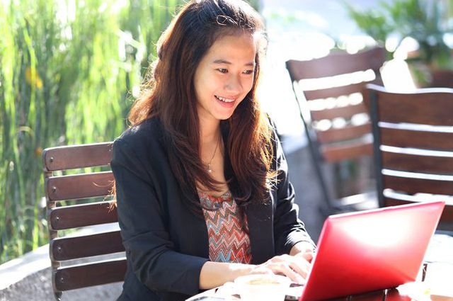 Woman sits outside on red laptop