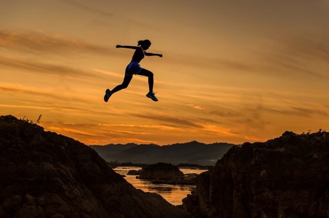 Person jumping over gap between rocks