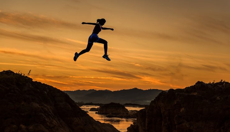 Person jumping over gap between rocks