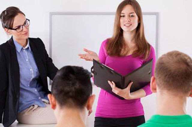 Woman with notebook asks two boys questions while another woman with glasses looks on