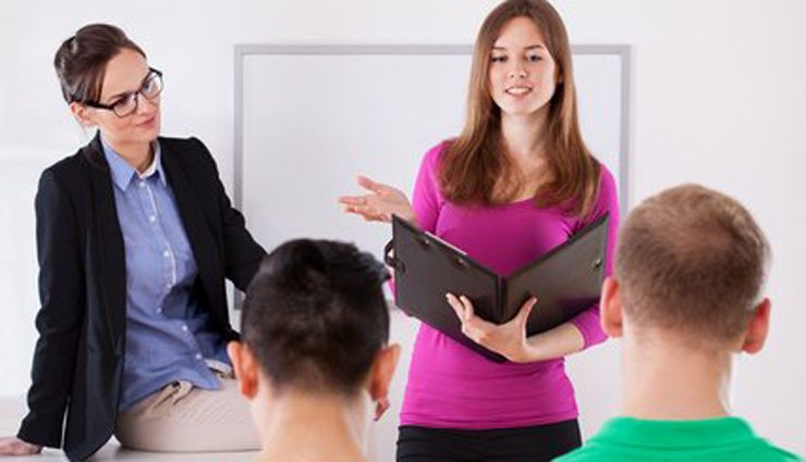 Woman with notebook asks two boys questions while another woman with glasses looks on