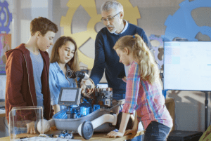 Male robotics teacher explains complicated robot to three students
