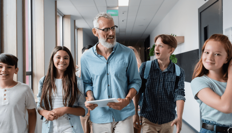 smiling male teacher with gray beard walking through hallway with four smiling middle school students