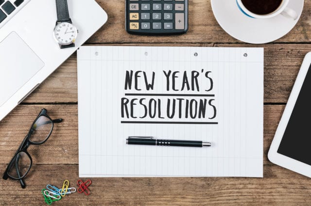 note with “new years resolution” text, Office desk with electronic devices, computer and paper