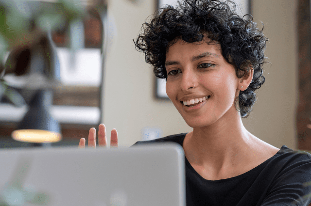 person with short hair facing a computer screen waving