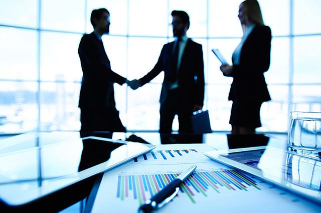 shadowed people in the background of a conference room shake hands