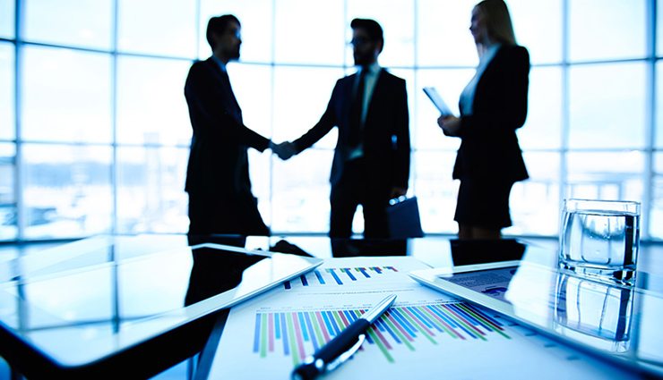 shadowed people in the background of a conference room shake hands