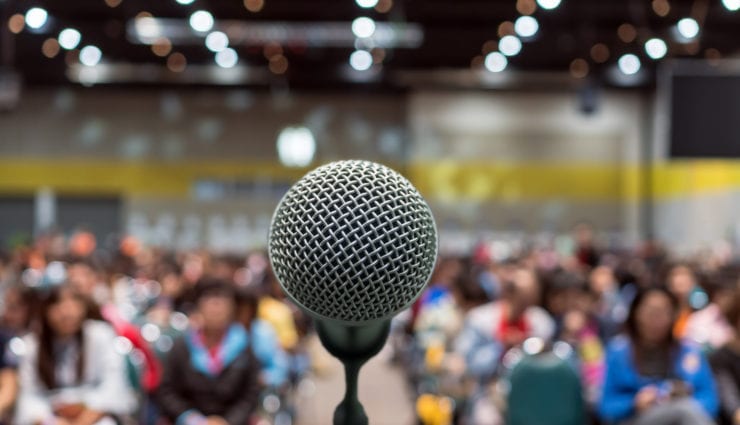 Microphone over photo of conference hall or seminar room in Exhibition Center background with Speakers on the stage and attendee background