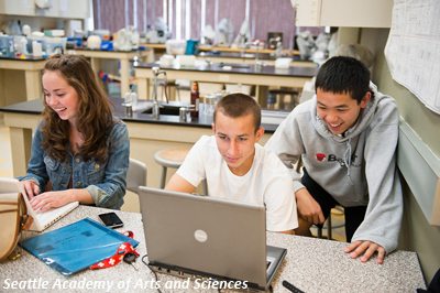 three high school students in science lab laughing with laptop