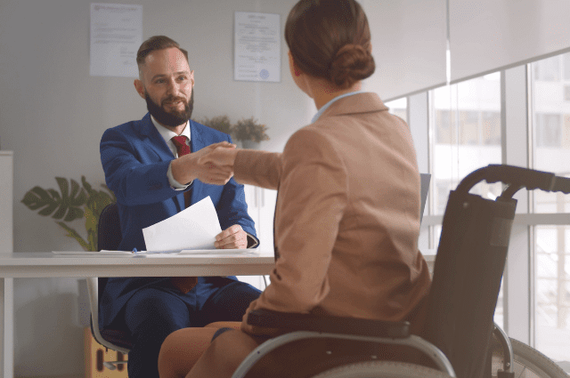 Seated man shaking hands across the desk with a woman in a wheelchair