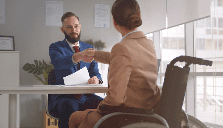 Seated man shaking hands across the desk with a woman in a wheelchair