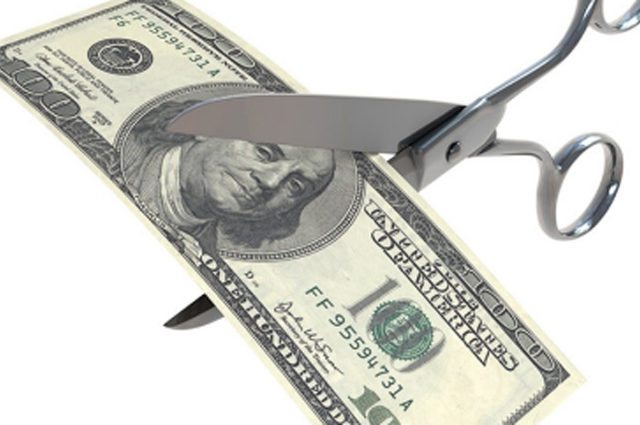 large silver metal scissors cut through a $100 bill