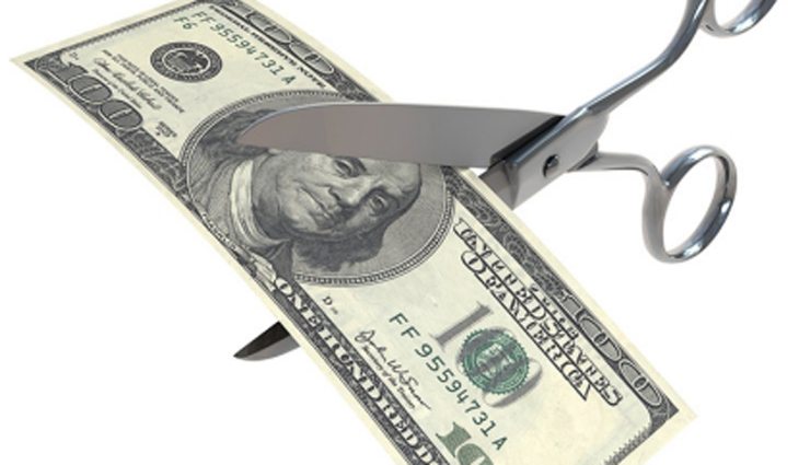 large silver metal scissors cut through a $100 bill
