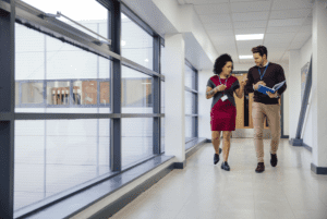 A female school leader and a younger male teacher walk down a school hallway