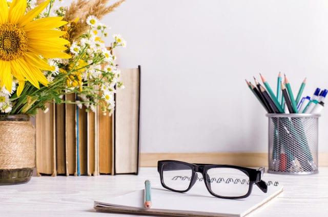 Books, glasses, markers and a bouquet of flowers in a vase on white board background. Concept for teachers day and first September