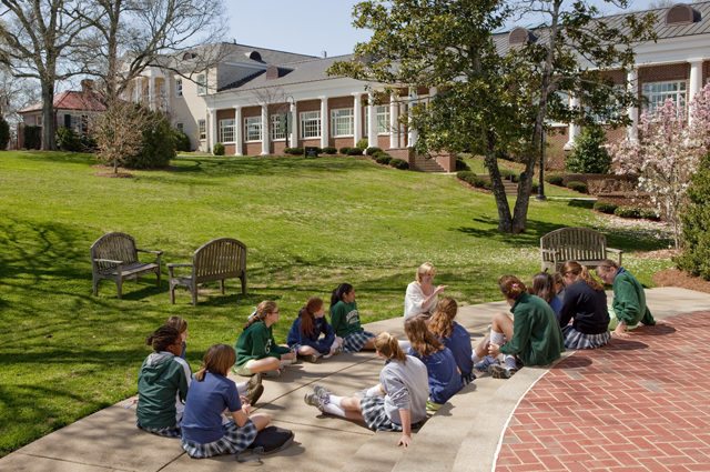 Woman leads group of uniformed female students outside on a beautiful campus