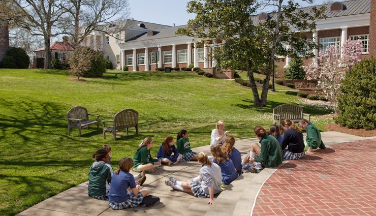 Woman leads group of uniformed female students outside on a beautiful campus