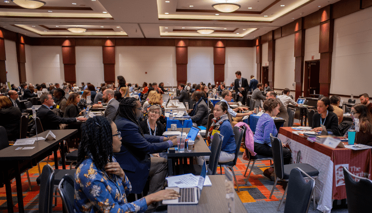 large ballroom full of small tables with people interviewing and conversating