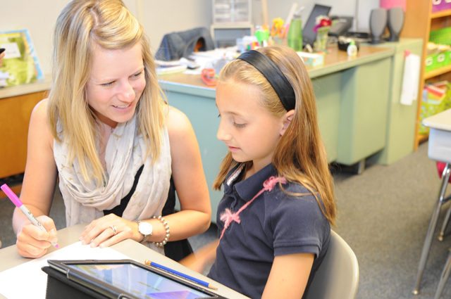 Female teacher discusses paper with elementary female student