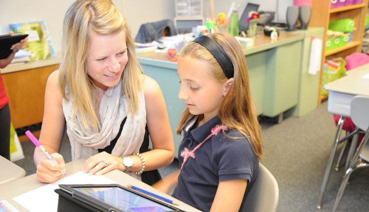 Female teacher discusses paper with elementary female student