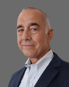 Man in a suit and checkered shirt smiling against a gray background.