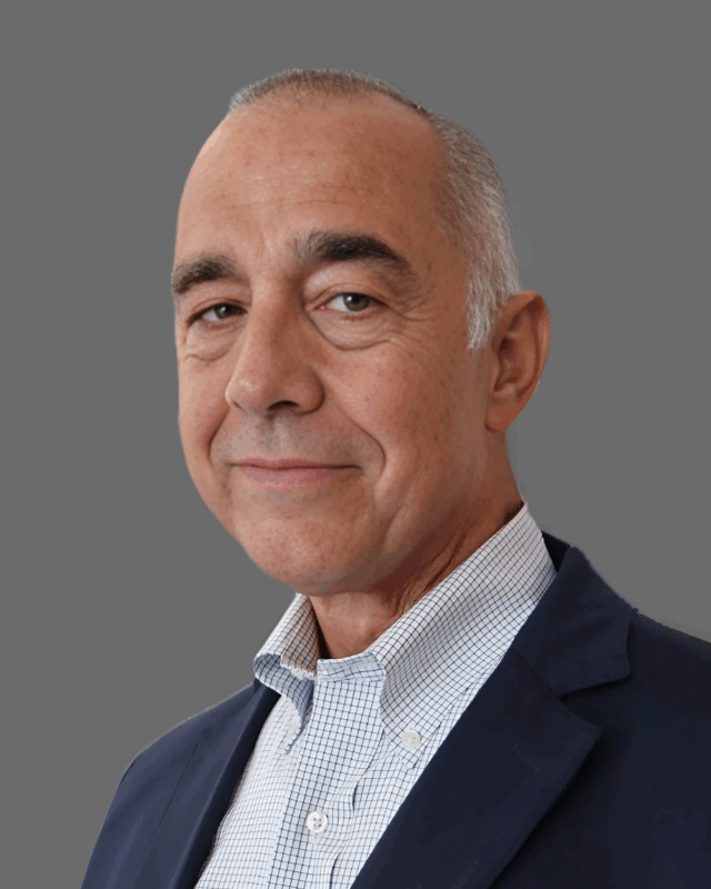 Man in a suit and checkered shirt smiling against a gray background.