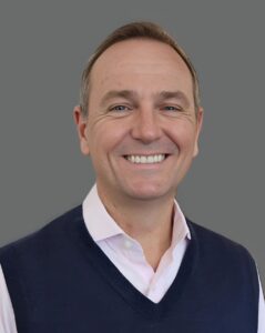 Smiling person in a vest and shirt against a gray background.