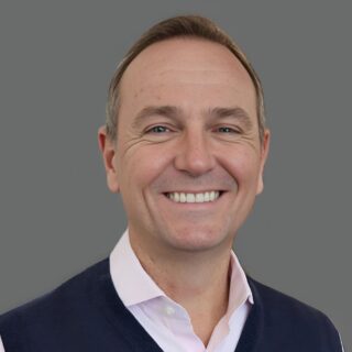 Smiling person in a vest and shirt against a gray background.