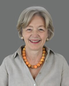 Smiling woman with short gray hair and orange necklace against a gray background