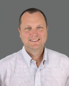 Smiling person wearing a patterned shirt against a gray background.