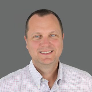 Smiling person wearing a patterned shirt against a gray background.
