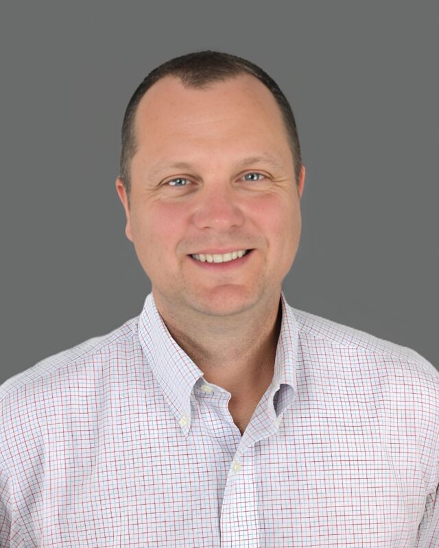 Smiling person wearing a patterned shirt against a gray background.