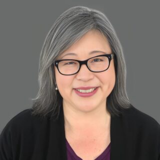 Smiling person with glasses and gray hair against a gray background.