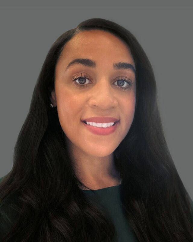 Smiling person with long dark hair against a gray background.