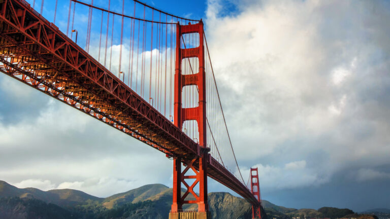Golden Gate Bridge spanning across bay with hills in the background under a partly cloudy sky.