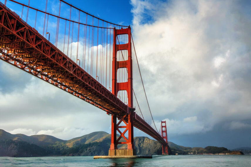 Golden Gate Bridge spanning across bay with hills in the background under a partly cloudy sky.