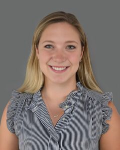 Smiling person wearing a striped blouse against a gray background.