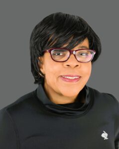 Woman wearing glasses and black top against a gray background.